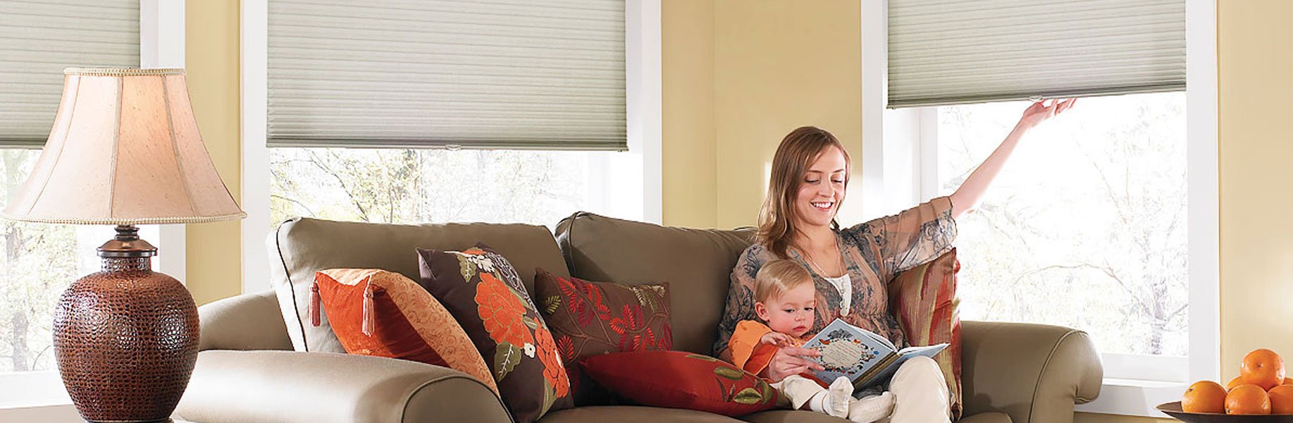 A mother and her baby reading on a sofa under cordless cellular shades